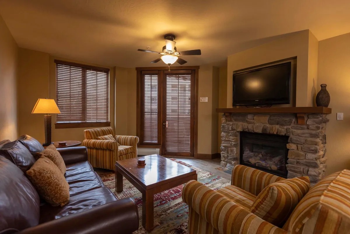 An inviting living room scene featuring a plush sofa, a cozy gas fireplace as the focal point, a coffee table, and expansive windows offering mountain views. The atmosphere is warm and ideal for relaxing or socializing after a day on the slopes.