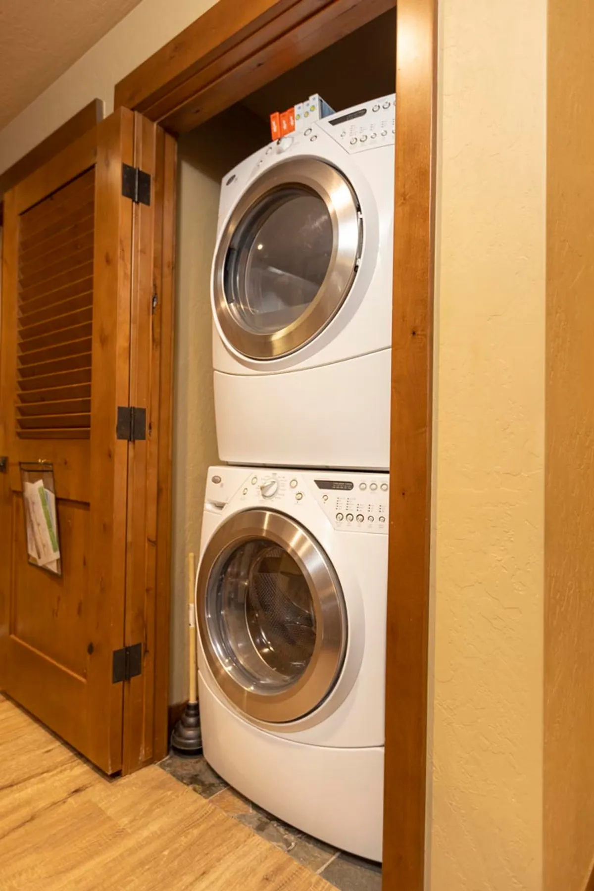 A practical in-unit laundry area with a stacked washer and dryer, wooden door, and informational papers attached for convenience. The organized setup is both functional and welcoming, supporting everyday needs during a stay.