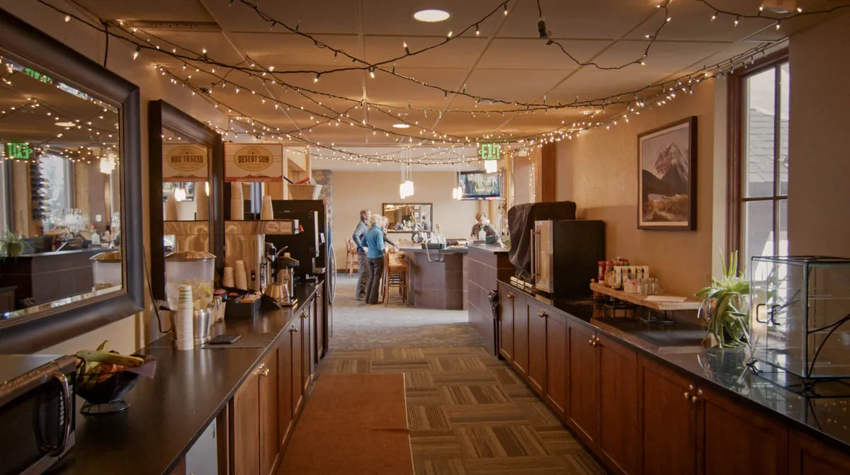 A stylish and comfortable lounge area with a coffee station, decorative lighting, and plush seating. The space is designed for socializing, relaxing with a beverage, or gathering before and after mountain adventures.