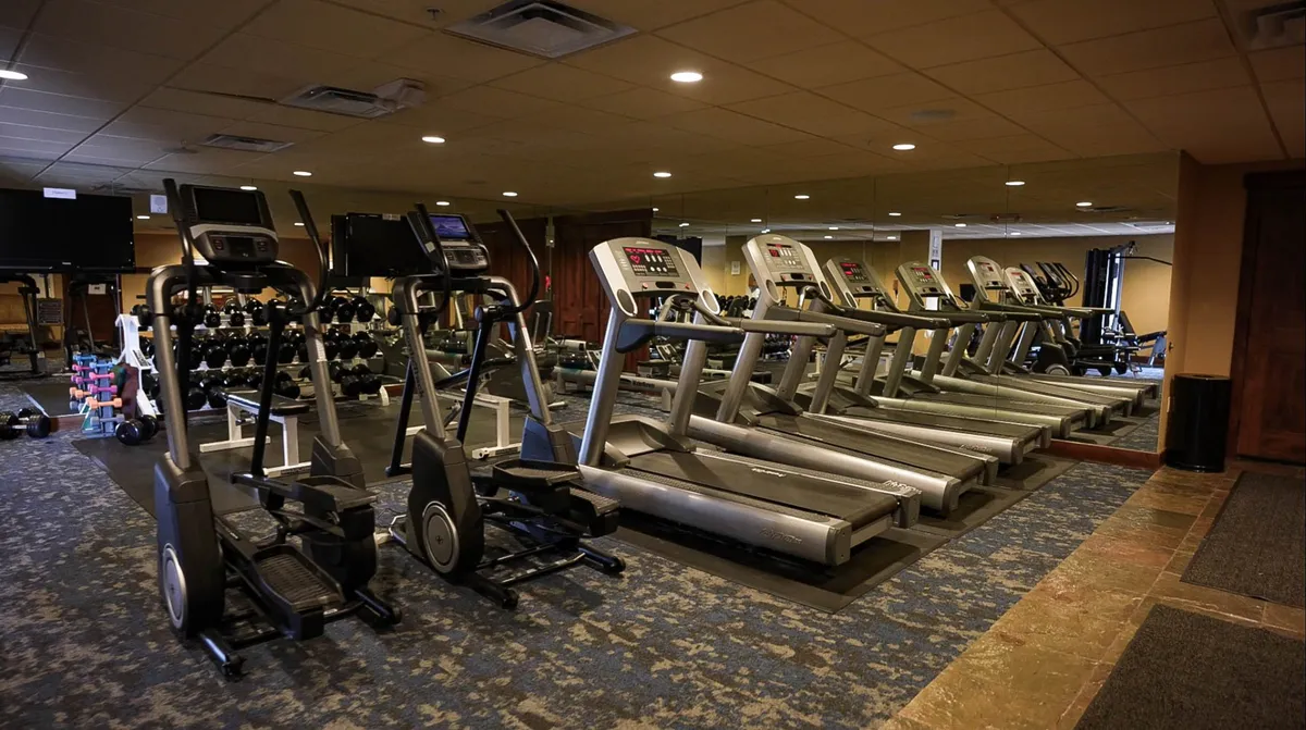 A modern, well-equipped fitness center featuring elliptical machines, treadmills, free weights, and a mirrored wall. The space is bright and energetic, ideal for maintaining fitness routines while on vacation.