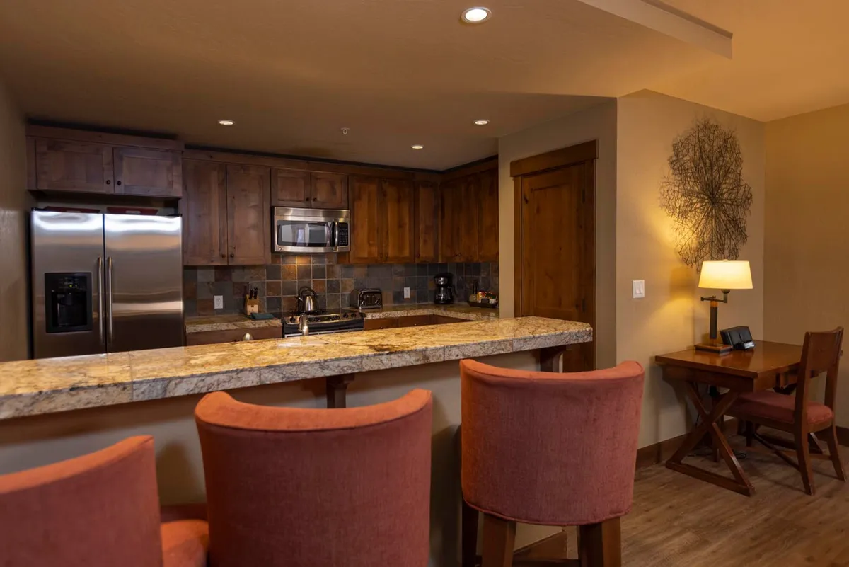 The photo focuses on the kitchen, showcasing granite countertops, wooden cabinetry, stainless steel appliances, and inviting bar stools. The space feels both functional and welcoming, making it ideal for preparing meals or gathering for a casual conversation.