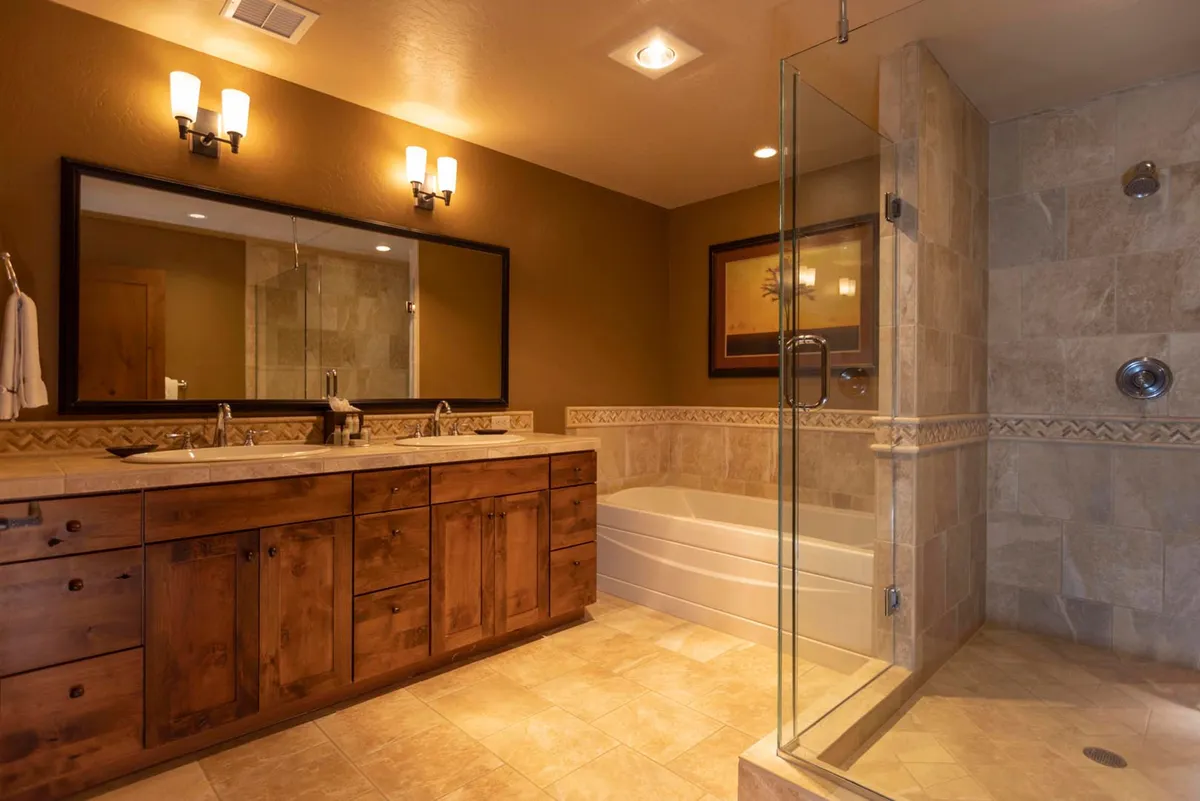 A luxurious, modern bathroom with a double sink vanity, glass shower enclosure, soaking tub, and framed artwork. Morning light streams in, creating a serene, spa-like environment ideal for unwinding after mountain adventures.