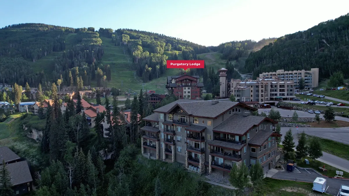 The majestic Purgatory Lodge stands at the base of the mountains, nestled among forests and other resort structures. The expansive backdrop emphasizes the resort’s stunning location and proximity to both adventure and relaxation.